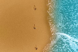 Top view of footprints on yellow golden sand and mint blue sea color. Drone photo of vacation. Copy space 
