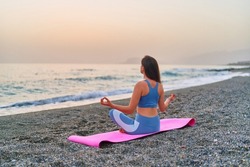 Back view of calm serene bliss satisfied fitness woman doing yoga meditation and breathing exercises on the beach by the sea. Mental mind care and healthy habits