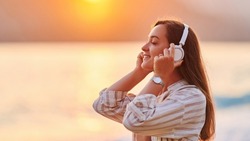 Calm serene alone woman with closed eyes enjoys of listening relax traveling music on the seashore at sunset time. Happy beautiful moment life 