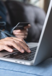 Woman sitting on sofa at home, hand holding credit card and using laptop computer for internet payment, digital banking and online shopping, E-commerce concept, closeup, toned image, vertical