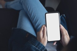 Mockup image of cell phone. Woman hand holding and using blank white screen mobile phone. Female hipster in blue jeans using and looking at empty mobile smartphone screen, mock up template