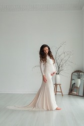 pregnant young woman wearing white long dress in light studio. beautiful maternity photoshoot. future mother elegant style with copy space for text