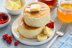 Fluffy Japanese Souffle pancakes with honey, red currants and banana on a white plate. Asian dessert for breakfast. Selective focus