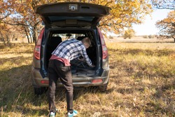  a male tourist in the forest opens the car trunk to get some things inside