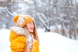 Outdoor close-up portrait of young beautiful happy smiling girl, wearing yellow jacket and knitted hat walking in winter park