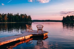 Two wooden chairs on a wood pier overlooking a lake at sunset in Finland