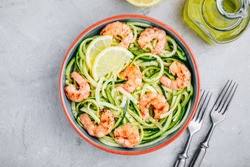 Spiralized zucchini noodles pasta with shrimps on gray stone background, top view