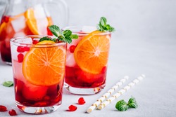 Pomegranate Orange Holiday Punch with ice and mint in glass on gray concrete stone background