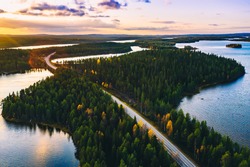 Aerial view of country road in green summer forest with blue lakes at sunset in Finland