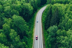 Aerial view of curved country road with cars and truck and green summer woods.