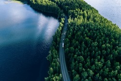 Aerial view of road in green woods and blue lakes water in summer Finland