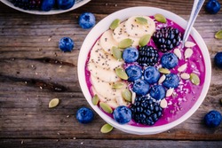 Purple smoothie bowl with fresh blackberries, blueberries, banana, sunflower seeds, pumpkin seeds, chia  seeds and coconut