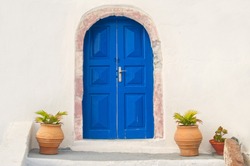 traditional white Greek house facade with blue door and flower pots, Santorini, Greece