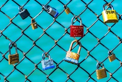 Colorful labeled padlocks/ locks locked on fence. Romantic relationship couples with names & special dates in writing. Love celebration and symbol of agreement, security, cherished moments and people.
