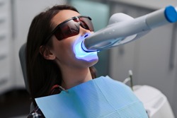 Close-up portrait of a female patient at dentist in the clinic. Teeth whitening procedure with ultraviolet light UV lamp.