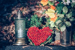 red heart decoration, burning candles and colorful floral decoration on grave in cemetery in autumn time