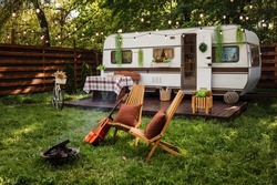 Camping season. Photo studio. Bicycle on the background of the trailer. Wooden chairs and a fire burns near them. Summer, green grass, recreation for people.