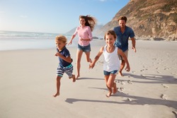 Parents Running Along Beach With Children On Summer Vacation