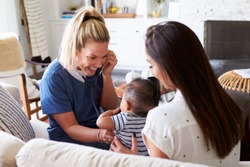 Female healthcare worker visiting a young mum and her infant son at home, using stethoscope