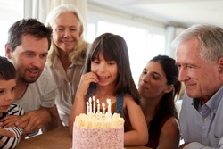 Three generation white family celebrating young girlâ€™s birthday with a cake and candles, close up