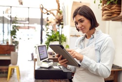 Female Owner With Digital Tablet Standing Behind Sales Desk Of Florists Store