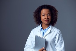 Studio Portrait Of Female Doctor In Lab Coat Holding Digital Tablet