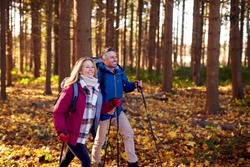 Side View Of Mature Retired Couple Walking Through Fall Or Winter Countryside Using Hiking Poles