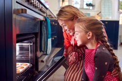Grandmother And Granddaughter Take Freshly Baked Cupcakes Out Of The Oven In Kitchen At Home