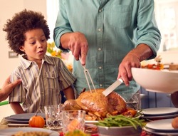 Grandson Watching Grandfather Carve Turkey As Family Celebrate Thanksgiving With Meal At Home