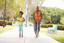 Grandmother And Granddaughter Riding Scooters In Park