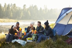 Group of friends sitting outside their tent near a lake