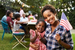 Black mother and baby hold flag at 4th July party, to camera