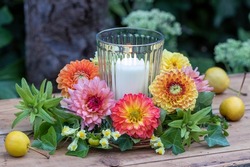 arrangement with wreath of dahlias, true toadflax and ivy and candle in glass
