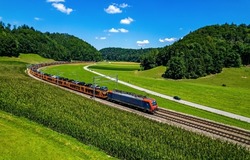 A freight train transports cars through the green valley in summer. Train ride on railway track. Train on railroad. Railroad train scene