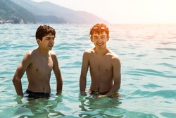 Two cute Caucasian boys are bathing in the sea of Monterosso, Liguria, Italy. They are enjoying the moment of relaxation and fun: they smile happily while they are in the water. Sun rays.