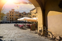 Lucca, Tuscany, Italy. August 2020. Amazing view from one of the entrances to the amphitheater square. A bike parked on the wall, the tables of a restaurant.