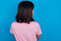 The back view of young asian woman wearing pink t-shirt against blue background Studio Shoot.
