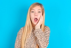 Shocked little caucasian kid girl wearing animal print sweater over blue background looks with great surprisment being very stunned, astonished with unexpected news, Facial expressions concept.