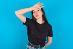 Young caucasian woman wearing black T-shirt over blue background wiping forehead with hand making phew gesture, expressing relief feels happy that he prevented huge disaster. It was close enough