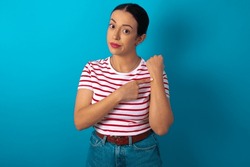 woman wearing striped T-shirt over blue studio background in hurry pointing to watch time, impatience, upset and angry for deadline delay