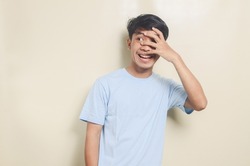 Portrait of asian young man wearing blue t-shirt glancing one eye on isolated background