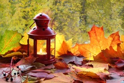 Colored autumn leaves and a red lantern with a candle on the window on an autumn yellow background. Space for text. The concept of autumn.