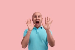 Frightened bald homosexual man with bristle, screams in fright, hold hands near face in protective gesture, has scared expression, gay friendly, wears blue polo shirt, poses over pink background