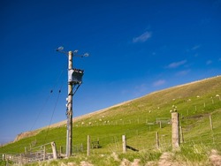 An electricity supply pylon delivering rural power through the UK national grid showing power cables, isolators and other equipment. Taken on a sunny day with a blue sky in Shetland, UK