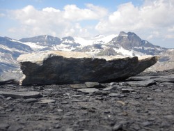 Focus on a rough granite rock with glaciers and craggy Alpine peaks in the background in Swiss Alps