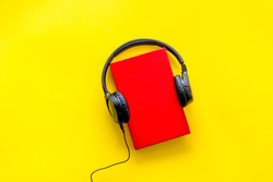 Audiobooks concept. Headphones put over hardback book. Yellow background top view copy space
