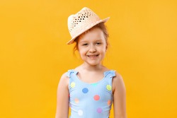 Happy cute beautiful charming little girl in a straw hat and a swimsuit. Closeup portrait of a baby on a yellow background.