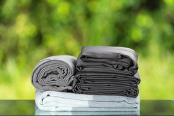 Stack of folded bedding. Monochrome gray gradient plaid towel bedsheet textile set on blurred foliage background.
