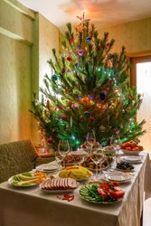 Festive Christmas served table against beautiful green pine tree decorated with many colorful new year toys. Xmas dinner, delicious food, christmas turkey. Winter holidays celebration at cozy home