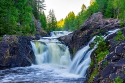 Beautiful landscape with waterfall in northern forest on summer evening. Powerful stream of water among stone rocks and green foliage. Kivach waterfall at Suna river in Karelia, Russia.